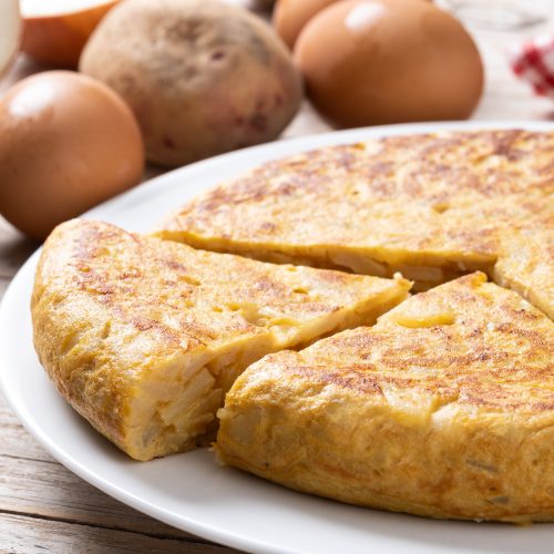 Traditional spanish omelette with ingredients on wooden table.